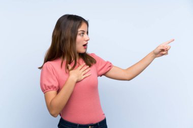 Genç esmer kız izole edilmiş mavi arka planda parmağını yana doğru gösteriyor.