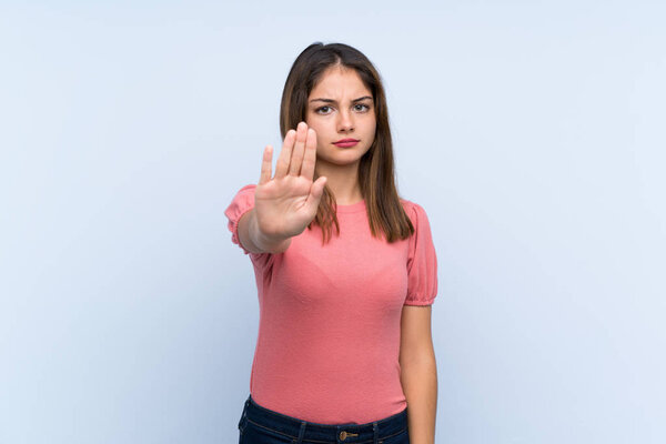 Young brunette girl over isolated blue background making stop gesture with her hand