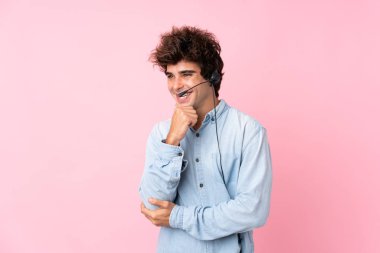 İzole edilmiş pembe geçmişi olan genç beyaz bir adam kulaklıkla çalışıyor.