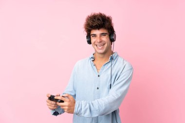 İzole edilmiş pembe arka planda video oyunlarında oynayan beyaz bir genç.