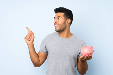 Büyük bir kumbara tutan izole arka plan üzerinde genç yakışıklı adam