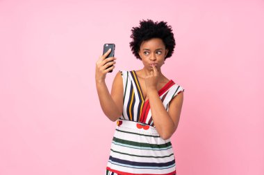 İzole edilmiş pembe arka planda Afrikalı Amerikalı bir kadın selfie çekiyor.