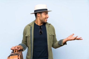 Soyutlanmış mavi arkaplan üzerinde antika bir evrak çantası tutan yakışıklı bir adam.