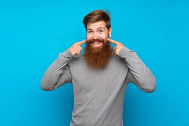 Kızıl saçlı, uzun sakallı, mavi arka planı olan mutlu ve hoş bir ifadeyle gülümseyen bir adam.
