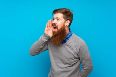 Uzun sakallı kızıl saçlı adam mavi arka planda ağzı sonuna kadar açık bağırıyor.