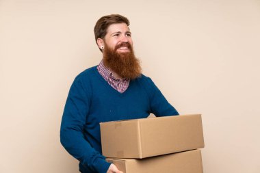 Kızıl saçlı, uzun sakallı, izole bir geçmişi olan bir adam başka bir yere taşımak için bir kutu tutuyor.