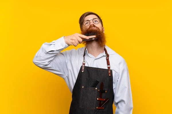 Barber s dlouhými vousy v zástěře nad izolovaným žlutým pozadím — Stock fotografie