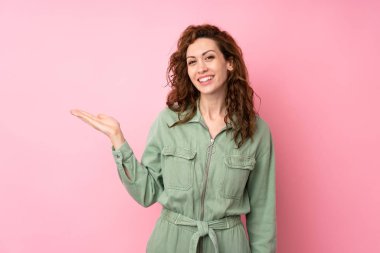 İzole edilmiş pembe arka plan üzerinde genç ve güzel bir kadın bir ilan vermek için avucunun içinde hayali bir alan tutuyor.