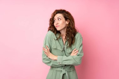 Soyutlanmış pembe arka planda genç ve güzel bir kadın omuzlarını kaldırırken şüphe jesti yapıyor.