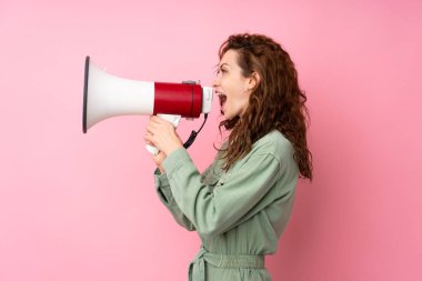 Young pretty woman over isolated pink background shouting through a megaphone clipart