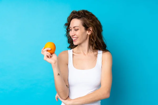 Ung Kvinna Med Lockigt Hår Håller Orange Över Isolerad Blå — Stockfoto