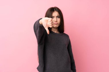 Soyutlanmış pembe arka planda genç bir kadın, olumsuz bir ifadeyle baş parmağını aşağı gösteriyor.