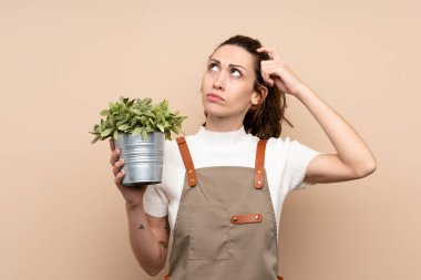 Bahçıvan kadın elinde bir bitki tutuyor. Şüpheleri var ve kafası karışmış bir yüz ifadesi var.