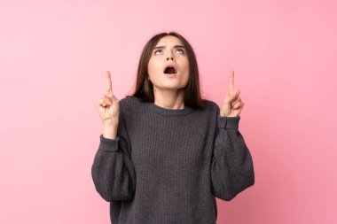 Soyutlanmış pembe arka planı olan genç bir kadın şaşırmış ve yukarı bakıyor.