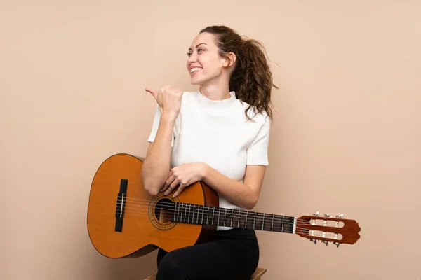 Young woman with guitar over isolated background pointing to the side to present a product