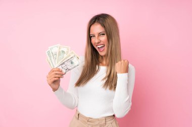 Young blonde woman over isolated pink background taking a lot of money clipart