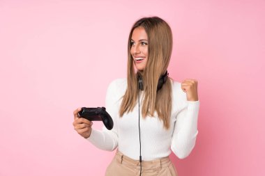 İzole edilmiş pembe arka planda video oyunlarında oynayan genç sarışın kadın.