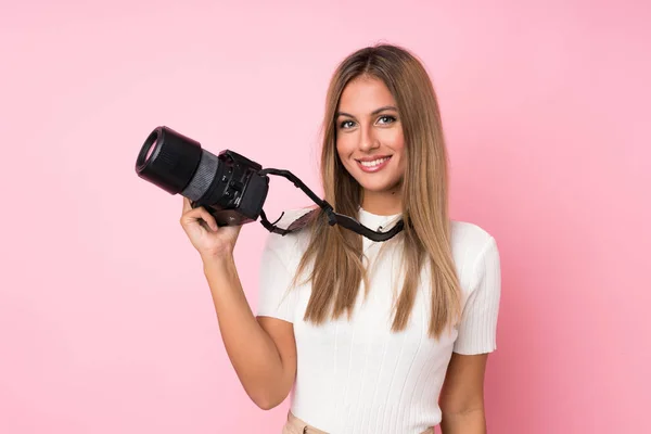 Mujer Rubia Joven Sobre Fondo Rosa Aislado Con Una Cámara —  Fotos de Stock