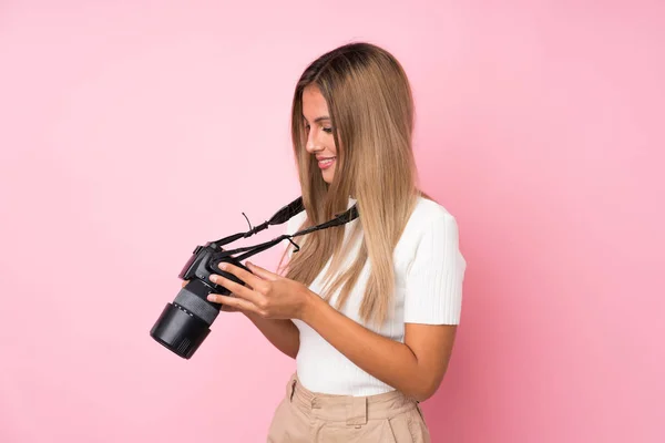 Mujer Rubia Joven Sobre Fondo Rosa Aislado Con Una Cámara —  Fotos de Stock