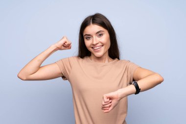 Kol saati ve şanslı ifadesiyle izole edilmiş mavi arka planı olan genç bir kadın.