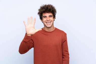 İzole edilmiş mavi arka planda genç beyaz adam parmaklarıyla beşi sayıyor.