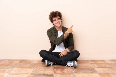 Genç, beyaz bir adam yerde oturmuş arkasını işaret ediyor.