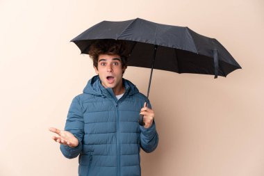 Şok olmuş bir yüz ifadesiyle izole edilmiş arka planda şemsiye tutan adam.
