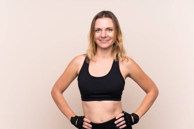 Sarışın sporcu kadın soyutlanmış arka planda kolları kalçasında ve gülümsüyor.