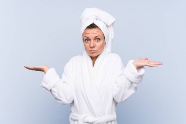 İzole edilmiş mavi arka planda bornozlu bir kadın. Kafası karışık bir yüz ifadesi olan bir kadın.