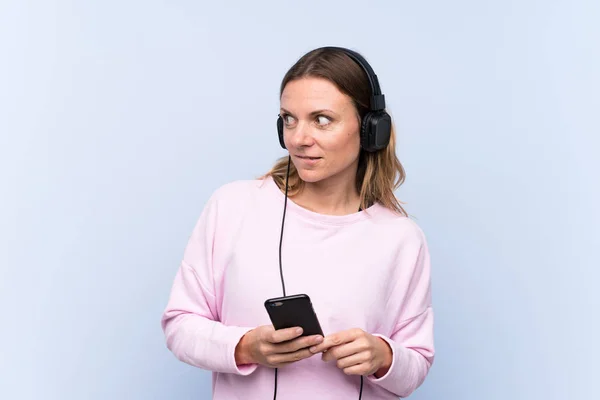 Женщина слушает музыку над изолированной голубой стеной — стоковое фото