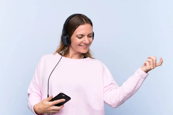 Žena poslouchá hudbu přes izolovanou modrou zeď — Stock fotografie