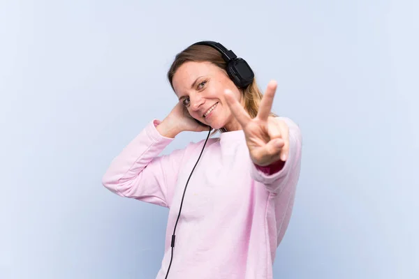 Kobieta słuchająca muzyki nad odizolowaną niebieską ścianą — Zdjęcie stockowe
