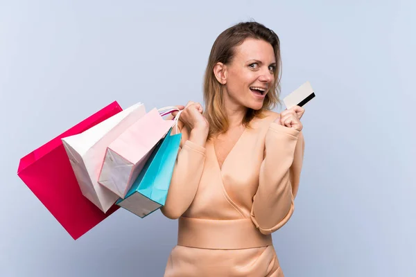 Blond Kvinna Över Isolerad Blå Bakgrund Håller Shoppingväskor Och Ett — Stockfoto