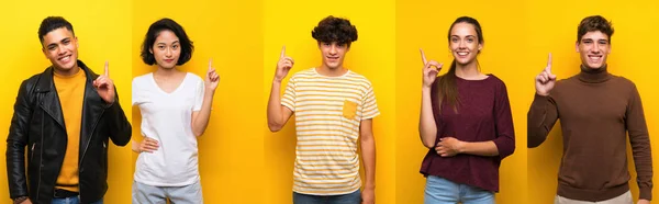 Set of people over isolated yellow background showing and lifting a finger in sign of the best