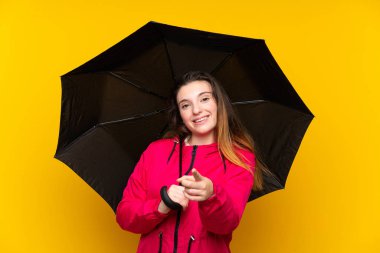 Sarı arka planda şemsiyesi olan esmer genç kız kendine güvenen bir ifadeyle seni işaret ediyor.