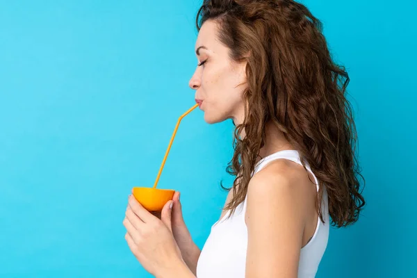 Ung kvinna med lockigt hår håller en orange över isolerad blå bakgrund — Stockfoto
