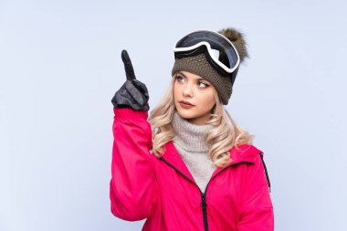 Kayakçı kız, kayak gözlükleriyle mavi arka planda şeffaf ekrana dokunuyor.