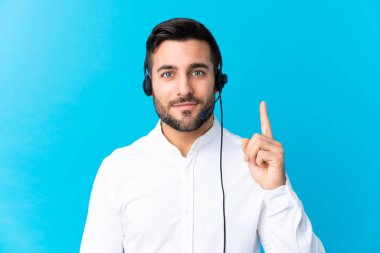 İzole edilmiş mavi arkaplan üzerinde kulaklıkla çalışan pazarlamacı adam işaret parmağıyla işaret etmek harika bir fikir.