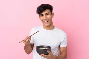 Arjantinli genç adam izole edilmiş beyaz arka planda elinde çubuklarla bir kase erişte tutuyor.