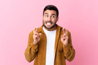 Sakallı, pembe arka planda kadife ceket giyen ve şans dileyen genç yakışıklı bir adam.