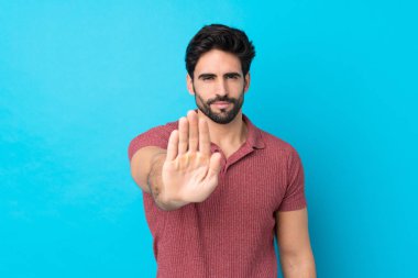 Sakallı, mavi arka planda genç ve yakışıklı bir adam dur işareti yapıyor.