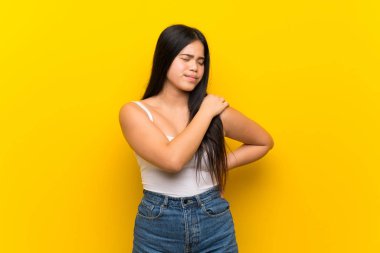 Genç Asyalı kız, sarı arka planda izole edilmiş, omuz ağrısından muzdarip, çabaladığı için.