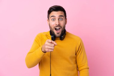 Soyutlanmış pembe arka planda kulaklıkları olan genç ve yakışıklı bir adam şaşırmış ve ön tarafı işaret ediyor.