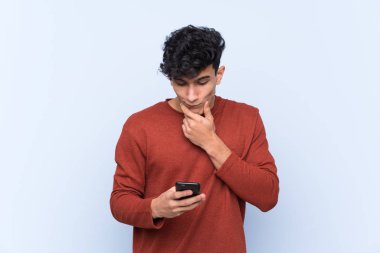 Arjantinli genç bir adam mavi arka plan üzerinde düşünüp bir mesaj gönderiyor.