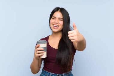 Asyalı genç bir kız, elinde güzel bir şey olduğu için başparmağıyla kahveyi kaldırıyor.