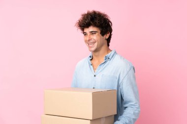 İzole edilmiş pembe arka planı olan genç beyaz bir adam başka bir yere taşımak için bir kutu tutuyor.