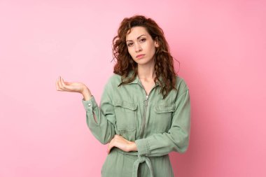 Soyutlanmış pembe arka planı olan genç ve güzel bir kadın bir şeyi anlamadığı için mutsuz.