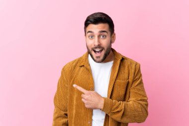 Pembe arka planda kadife ceket giyen sakallı yakışıklı genç bir adam.