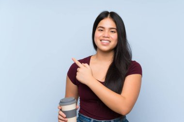 Genç Asyalı kız elinde kahve ile bir ürünü sunmak için kenarı işaret ediyor.