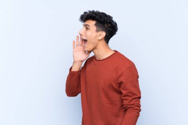 Arjantinli genç bir adam mavi arka planda ağzı sonuna kadar açık bağırıyor.